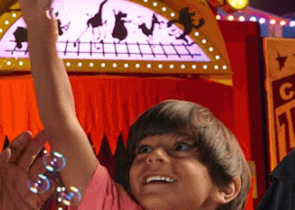 A family enjoys catching bubbles inside an amusement park with colorful circus-themed decorations and a "Madagascar: Mad Pursuit!" sign.