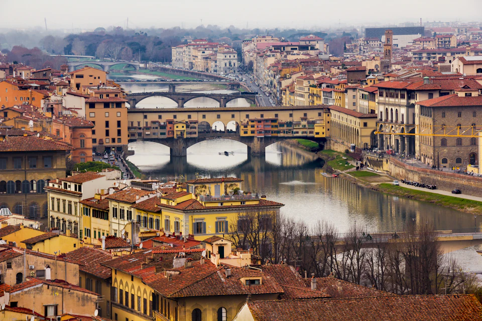 A scenic view of Florence, Italy, featuring the Ponte Vecchio bridge spanning the Arno River, surrounded by historic buildings.