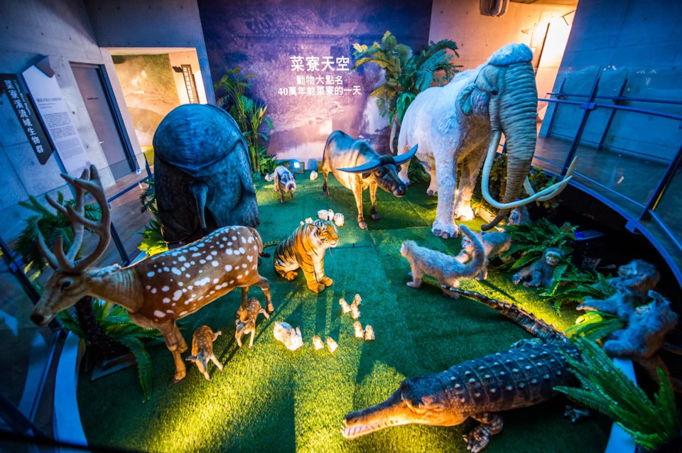 A display of animal statues, including an elephant, tiger, deer, and crocodile, set in a lush indoor exhibit with lighting.