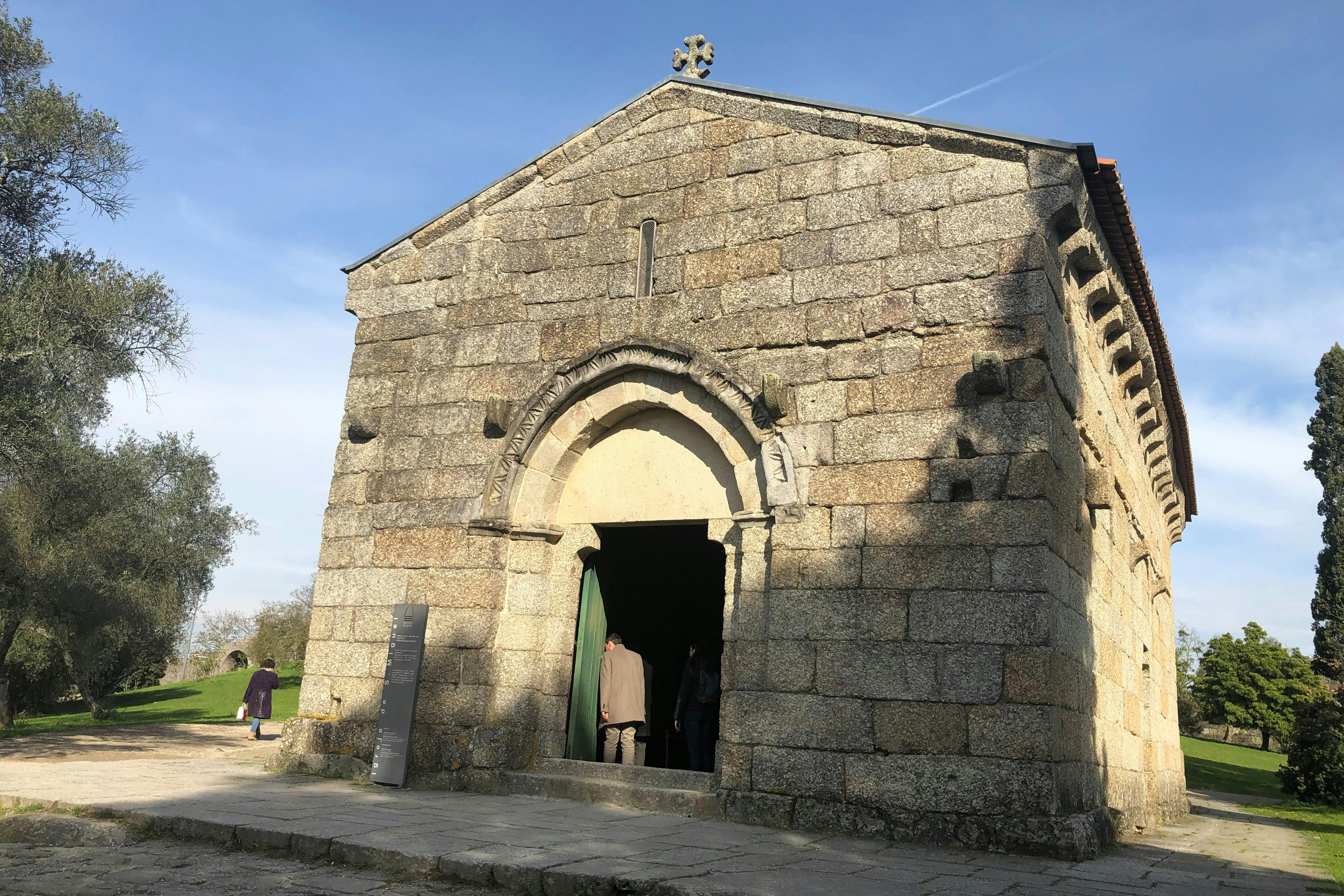 Stone building with an arched entrance, partially visible individuals near the doorway, and clear skies in the background.