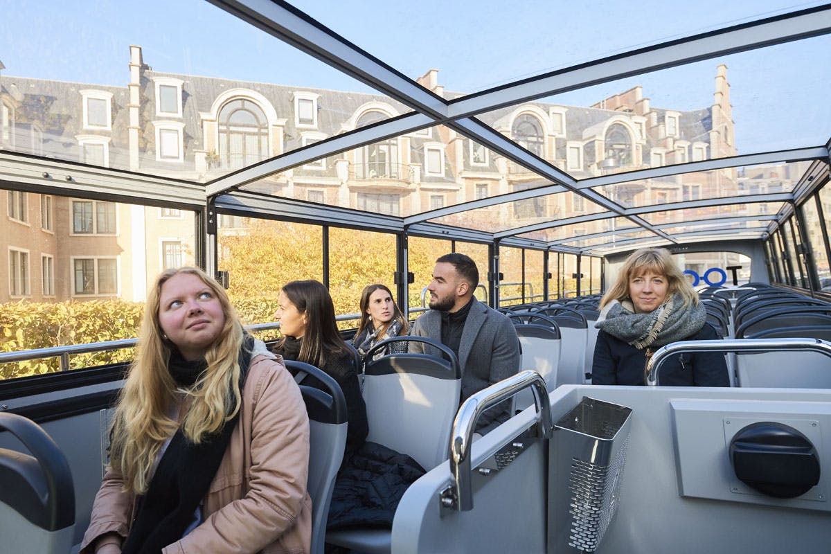 I passeggeri di un autobus turistico con tetto in vetro guardano gli edifici storici in stile europeo e il fogliame autunnale all'esterno.