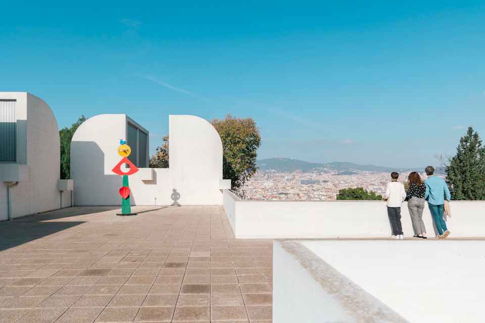 A rooftop terrace with modern sculptures, a person standing near the edge, and a cityscape visible in the background.