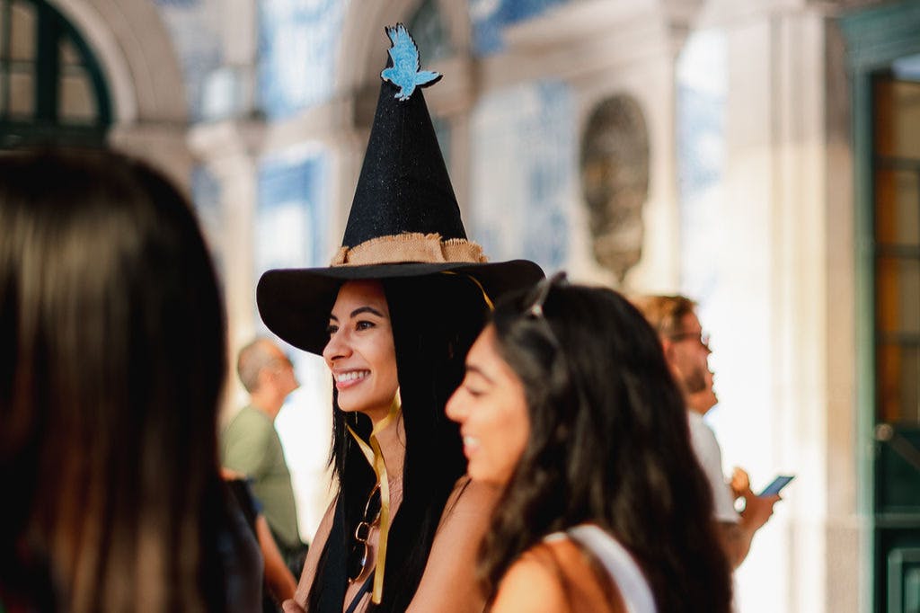 A girl wearing a black witch hat looks excited. The hat has a blue eagle on top.