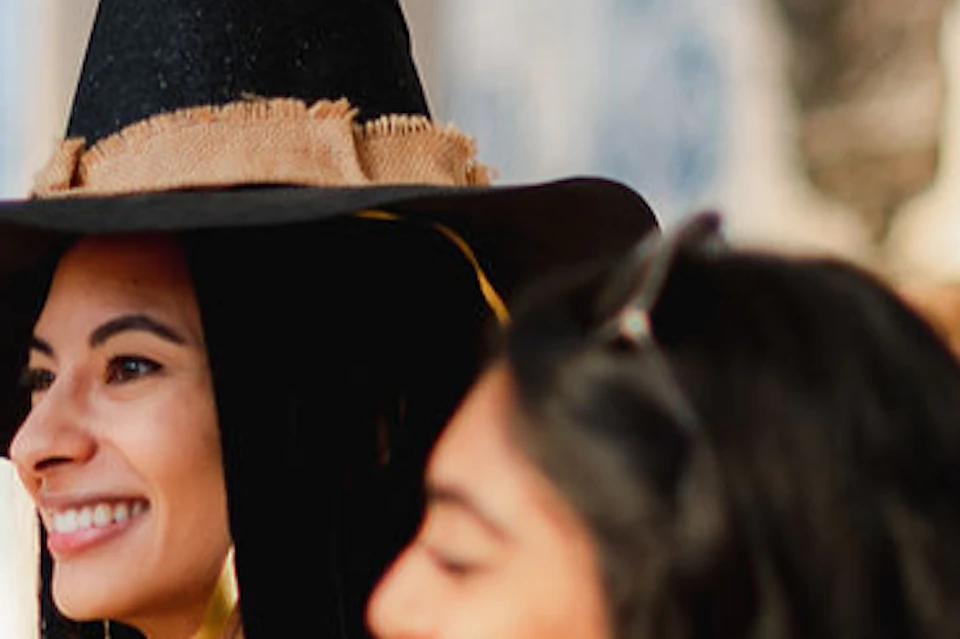A girl wearing a black witch hat looks excited. The hat has a blue eagle on top.