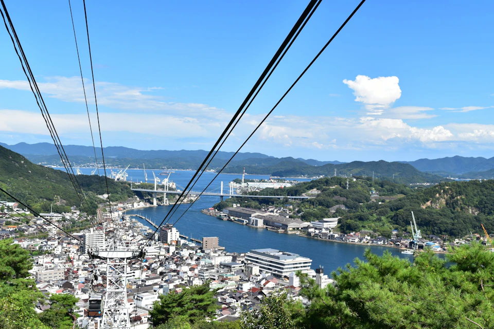 A cityscape with a river, bridges, and hills in the background, viewed from a high vantage point with cable lines visible.