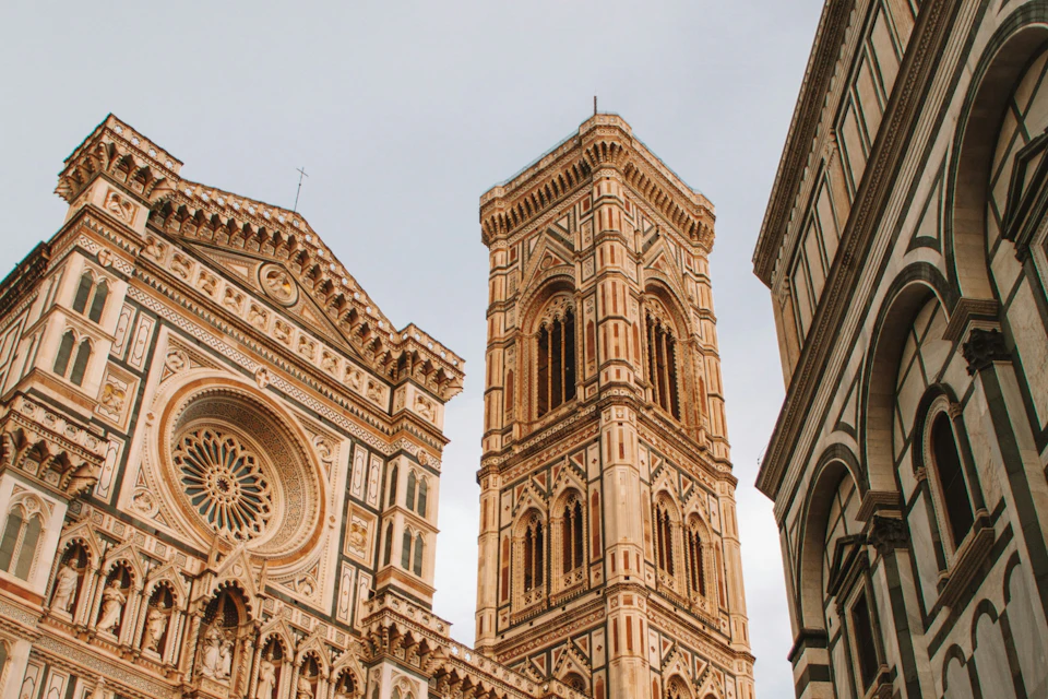 A detailed view of an ornate cathedral and bell tower with intricate patterns and carvings under a cloudy sky.
