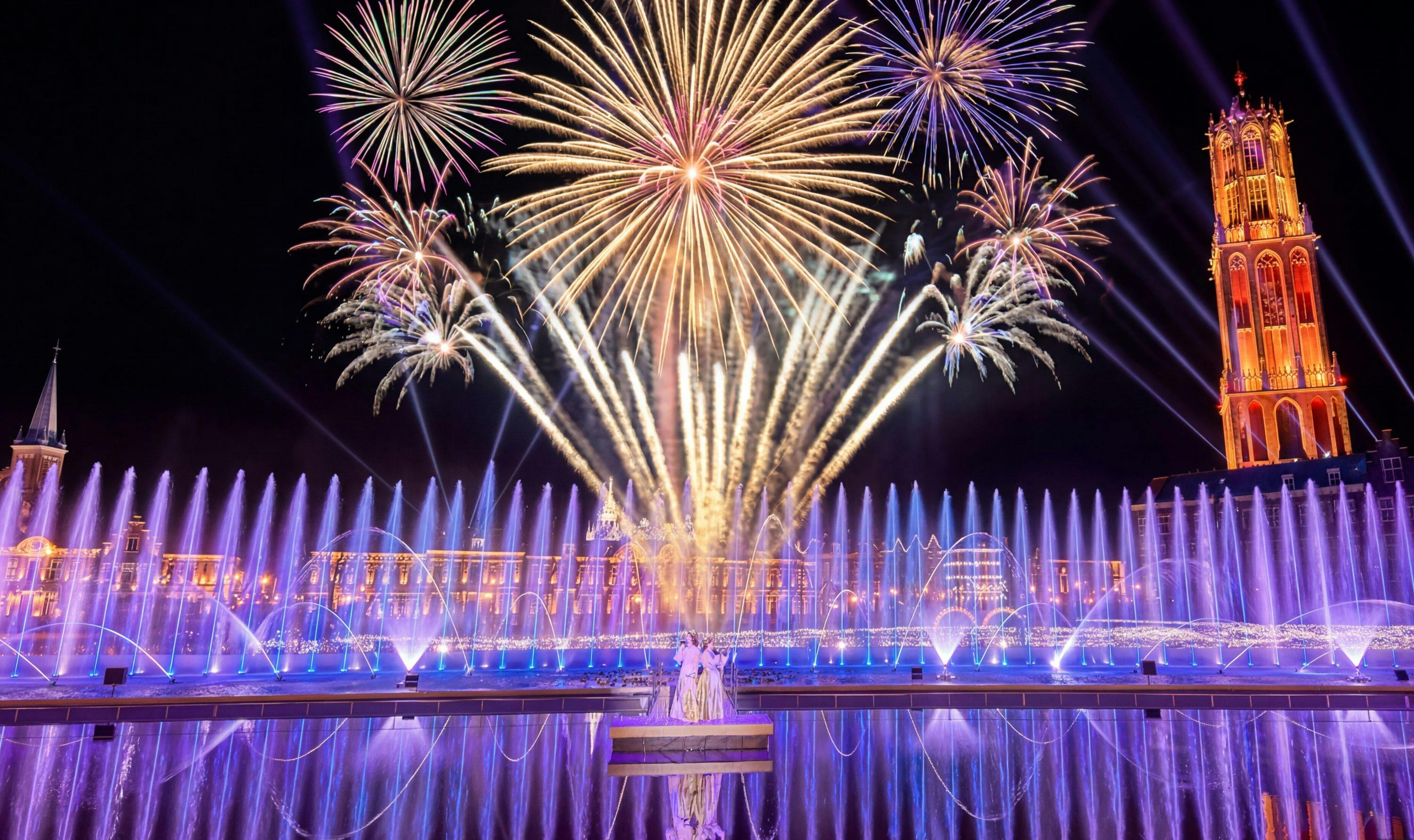 Des feux d'artifice éclatants illuminent le ciel nocturne au-dessus d'une fontaine illuminée, créant ainsi une ambiance animée et festive.