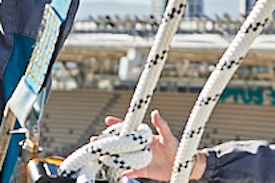 Two people in harnesses with raised arms smile while standing on a stadium roof, with empty stadium seats below them.