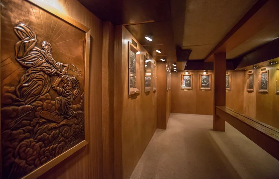 A dimly lit hallway with wooden panels displaying framed, decorative bronze reliefs under ceiling spotlights.