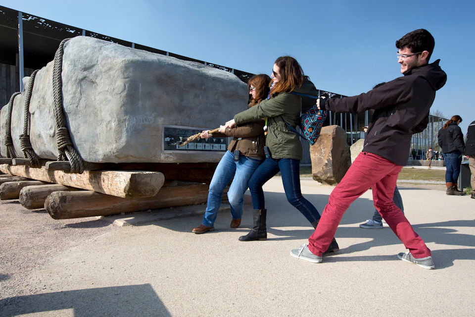 Three people smiling and pulling a rope together in an outdoor setting on a sunny day.