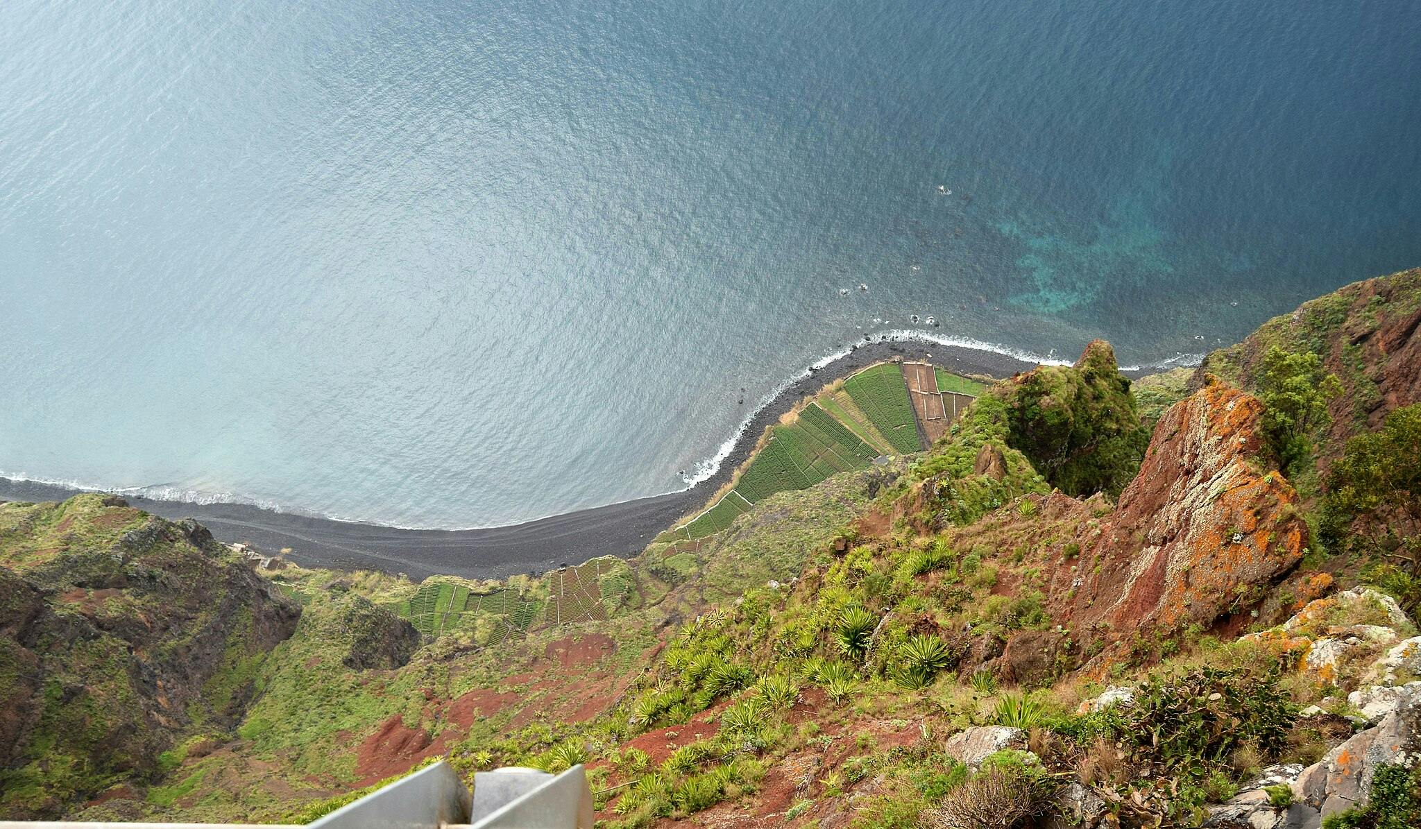 从悬崖上俯瞰弯曲的海岸线，黑色的沙滩，绿色的农田和郁郁葱葱的植被。