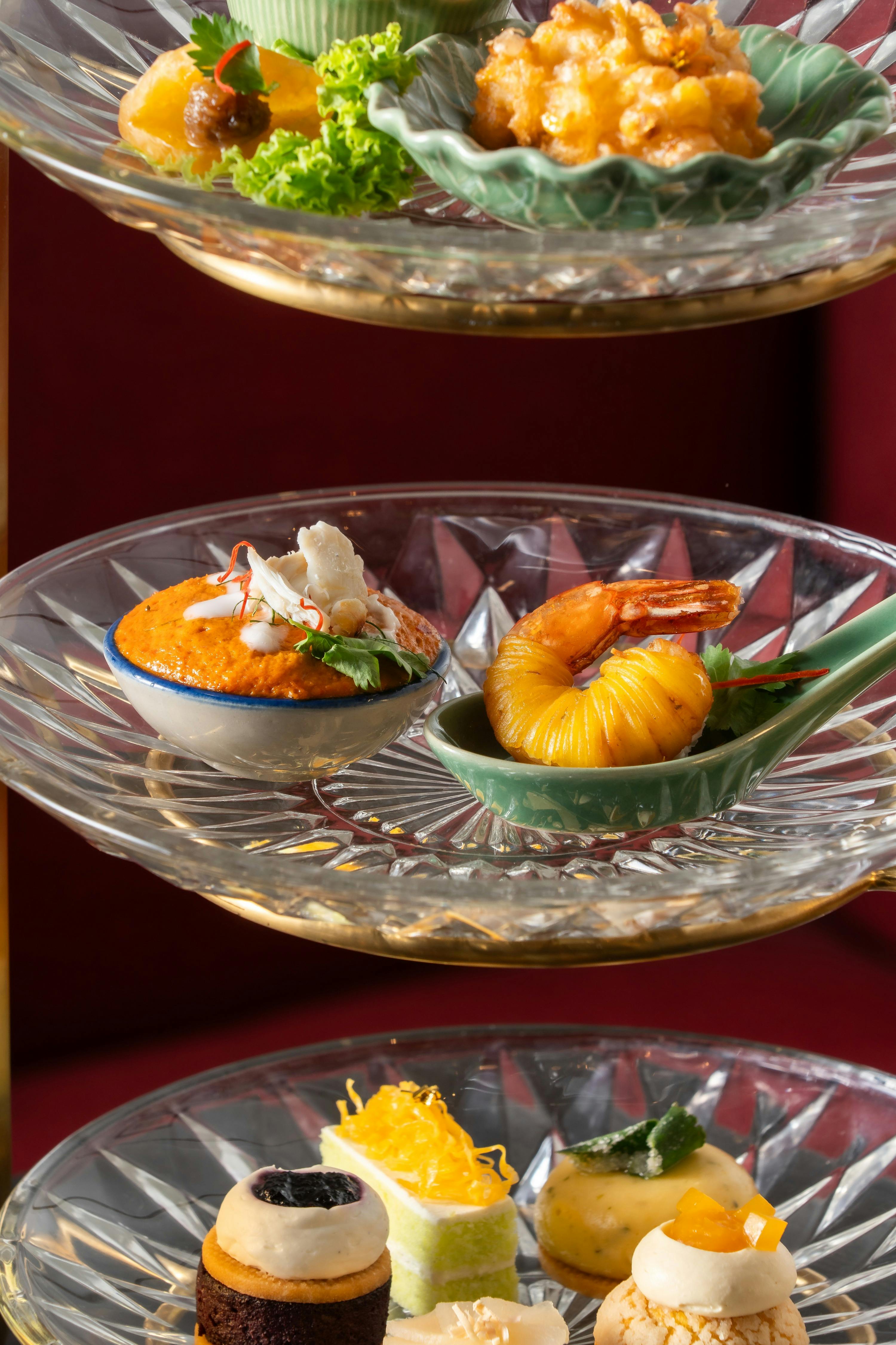 A glass plate with two dishes: a bowl of orange sauce garnished with herbs and shrimp, and a shrimp wrapped in pastry.