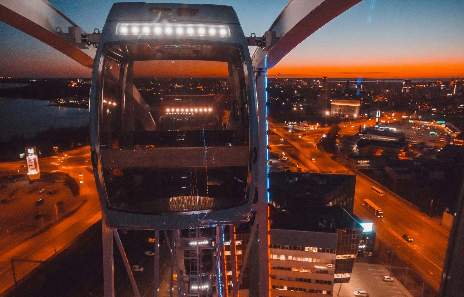 A Ferris wheel cabin at sunset, overlooking a cityscape with illuminated buildings and roads.