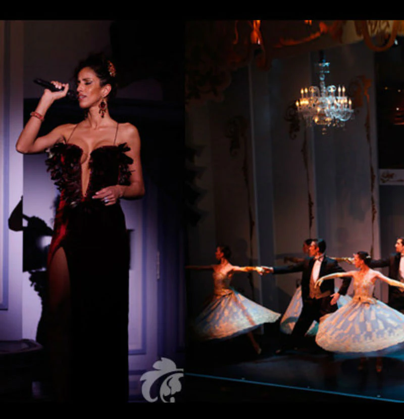 A woman sings on stage in a black dress, while dancers in formal attire perform under a chandelier.