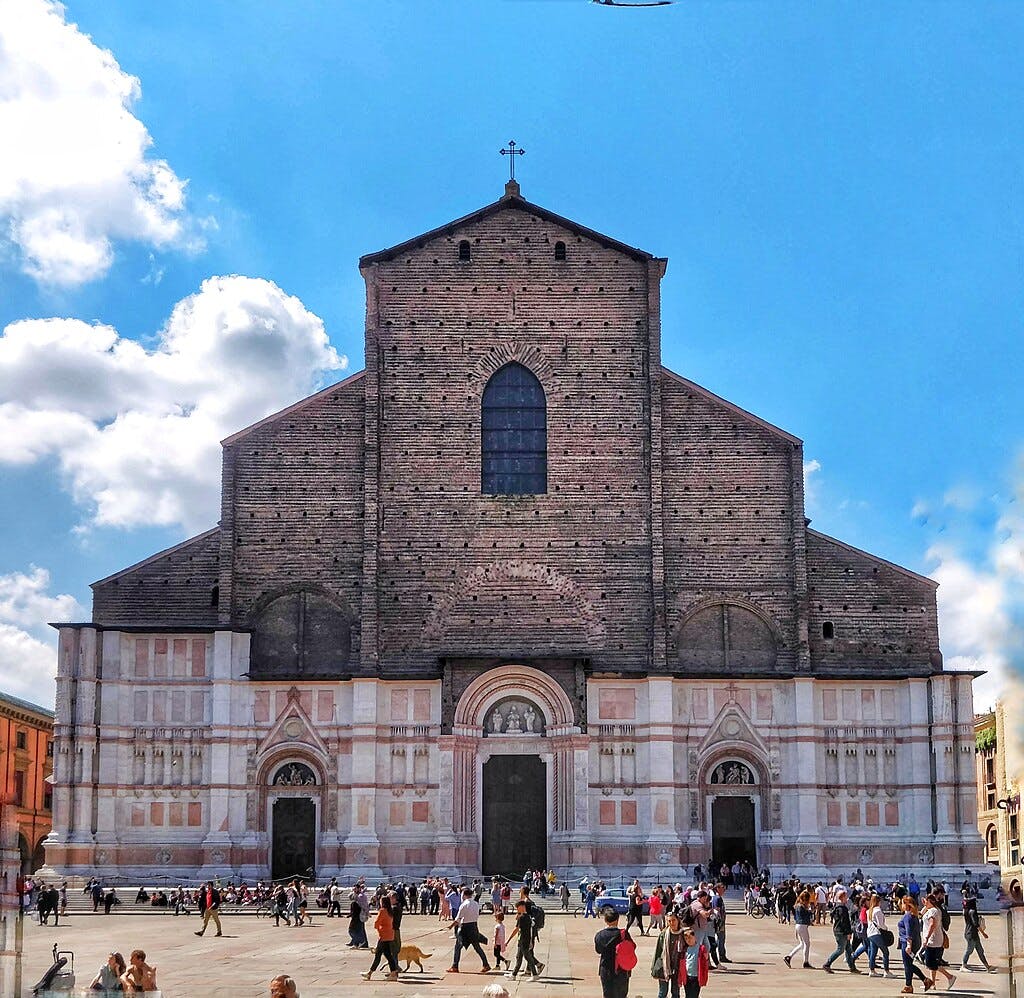 Grande façade d'église historique avec de nombreuses personnes marchant au premier plan sous un ciel bleu lumineux.