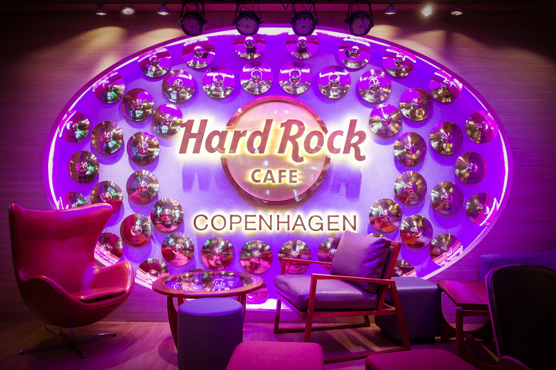 Vibrant seating area at Hard Rock Cafe Copenhagen, with 'Hard Rock Cafe' sign and decorative mirror discs on purple-lit wall.
