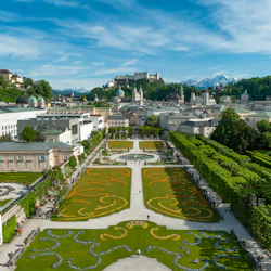 En flygfoto över en formell trädgård med invecklade blommönster, gångvägar och en stadsbild med historiska byggnader och en fästning på en kulle.
