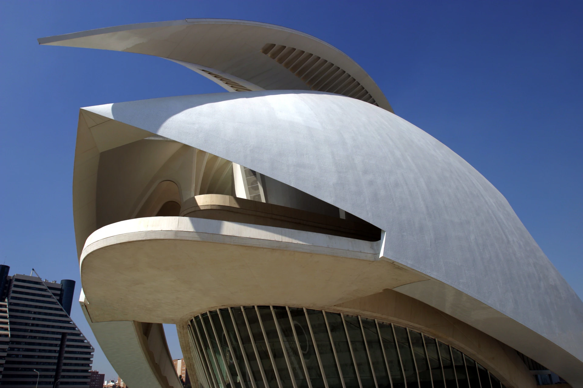 Modern building with curved, layered white structures and elongated horizontal windows against a clear blue sky.