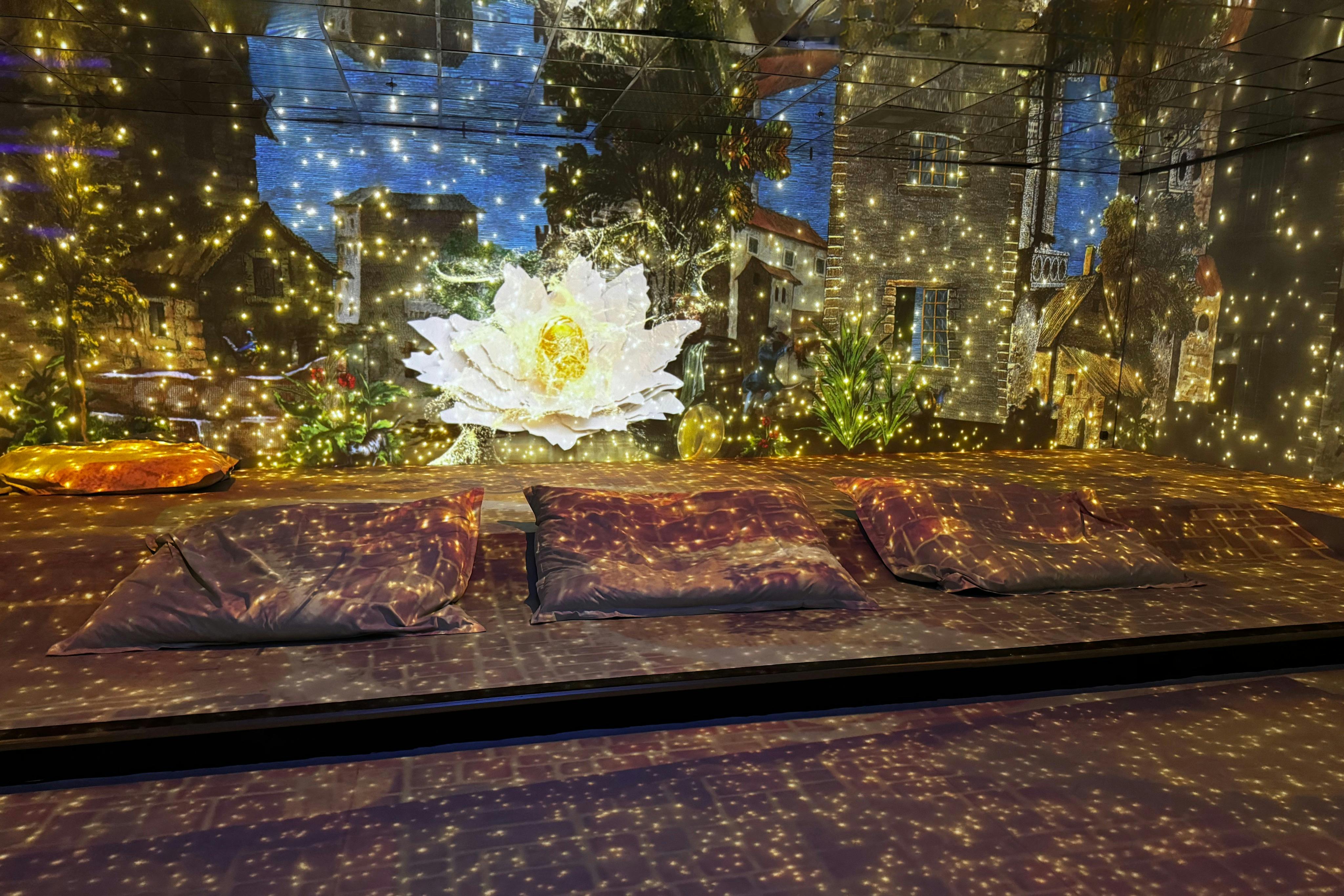 Three cushions on a floor with a background of a glowing flower, buildings, and twinkling lights.