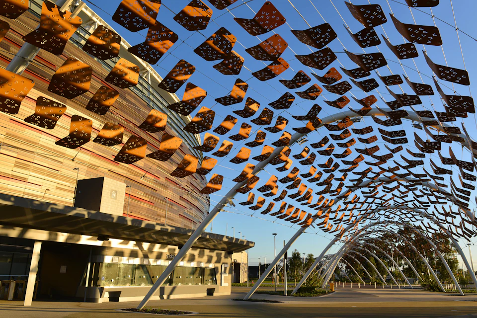A modern building with horizontal stripes stands next to an outdoor art installation of suspended square panels.
