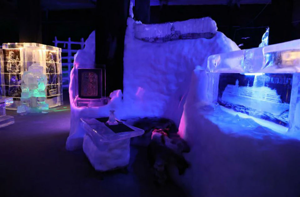 An ice room with ice furniture, including a table, sofa, and cabinets, illuminated by purple and blue lights.