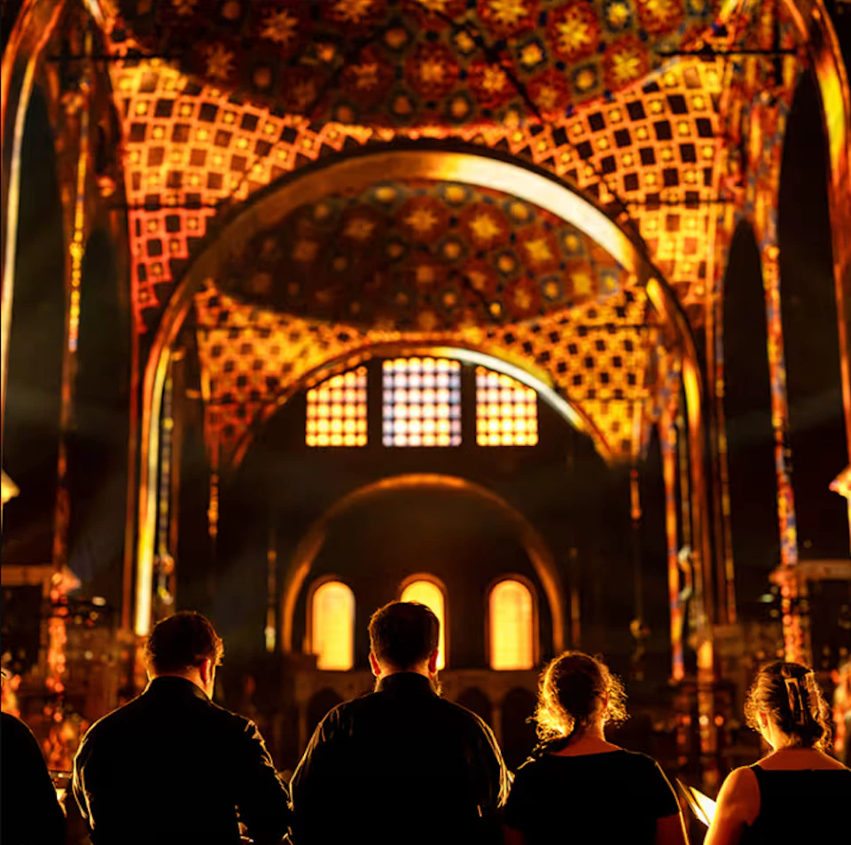 Five people in silhouette facing a brightly lit, ornate cathedral interior with colorful patterns and arched windows.