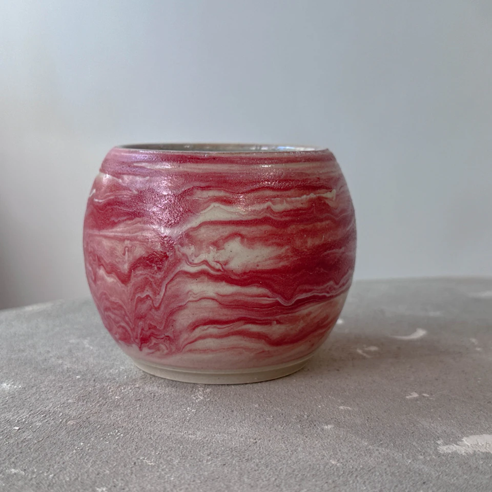 A round ceramic pot with a red and white marbled pattern, placed on a gray textured surface against a plain background.