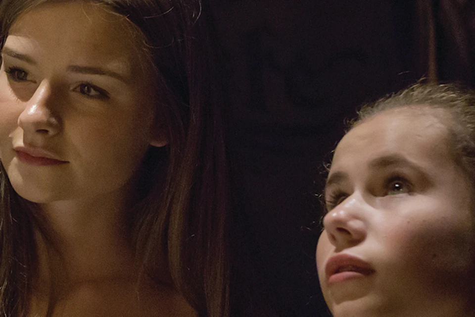 Two girls stand in a dimly lit room with walls decorated with numerous skulls arranged in patterns.