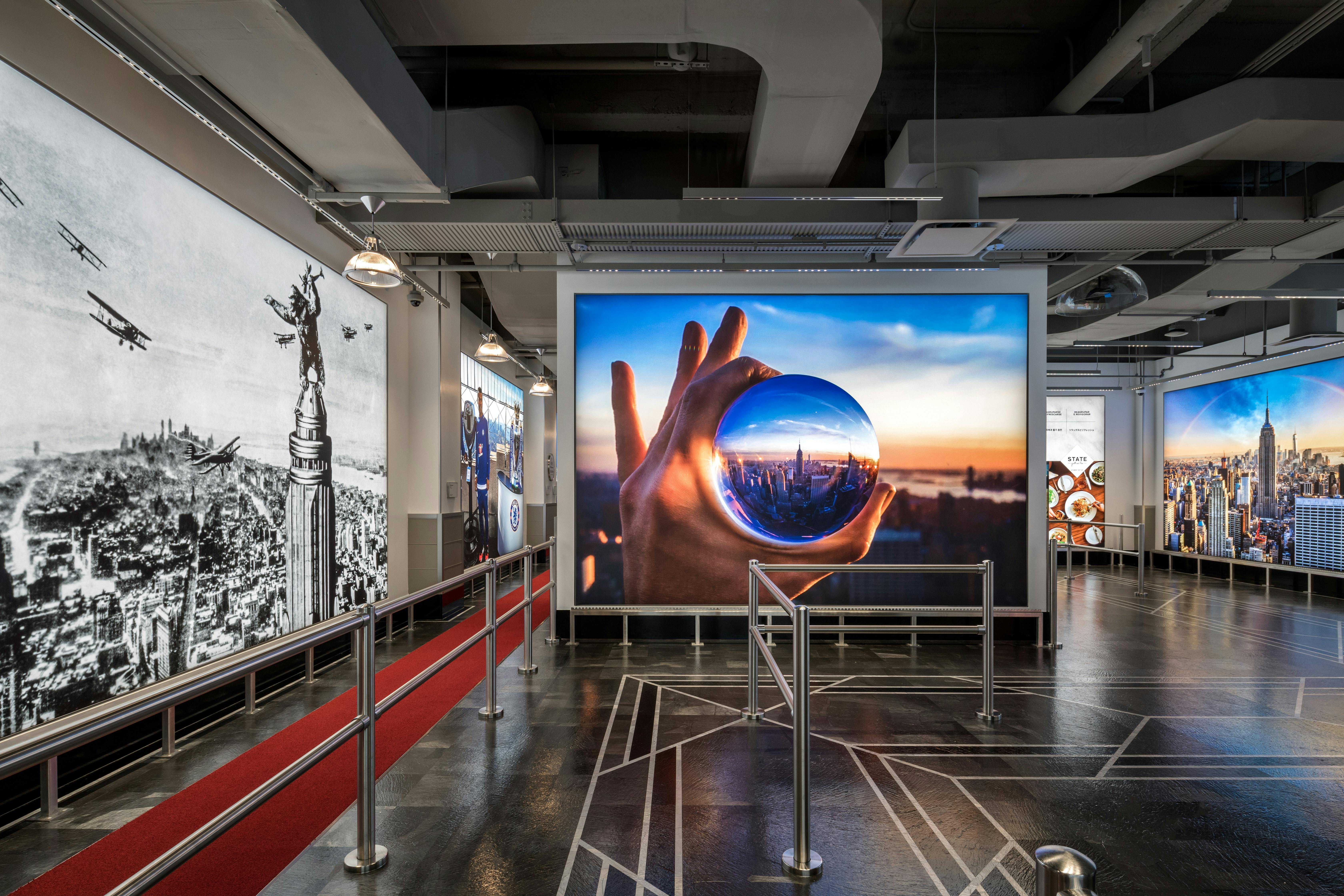 Galleria con un murale in bianco e nero della Statua della Libertà e una grande foto di una mano che tiene una sfera riflettente, raffigurante un paesaggio urbano.