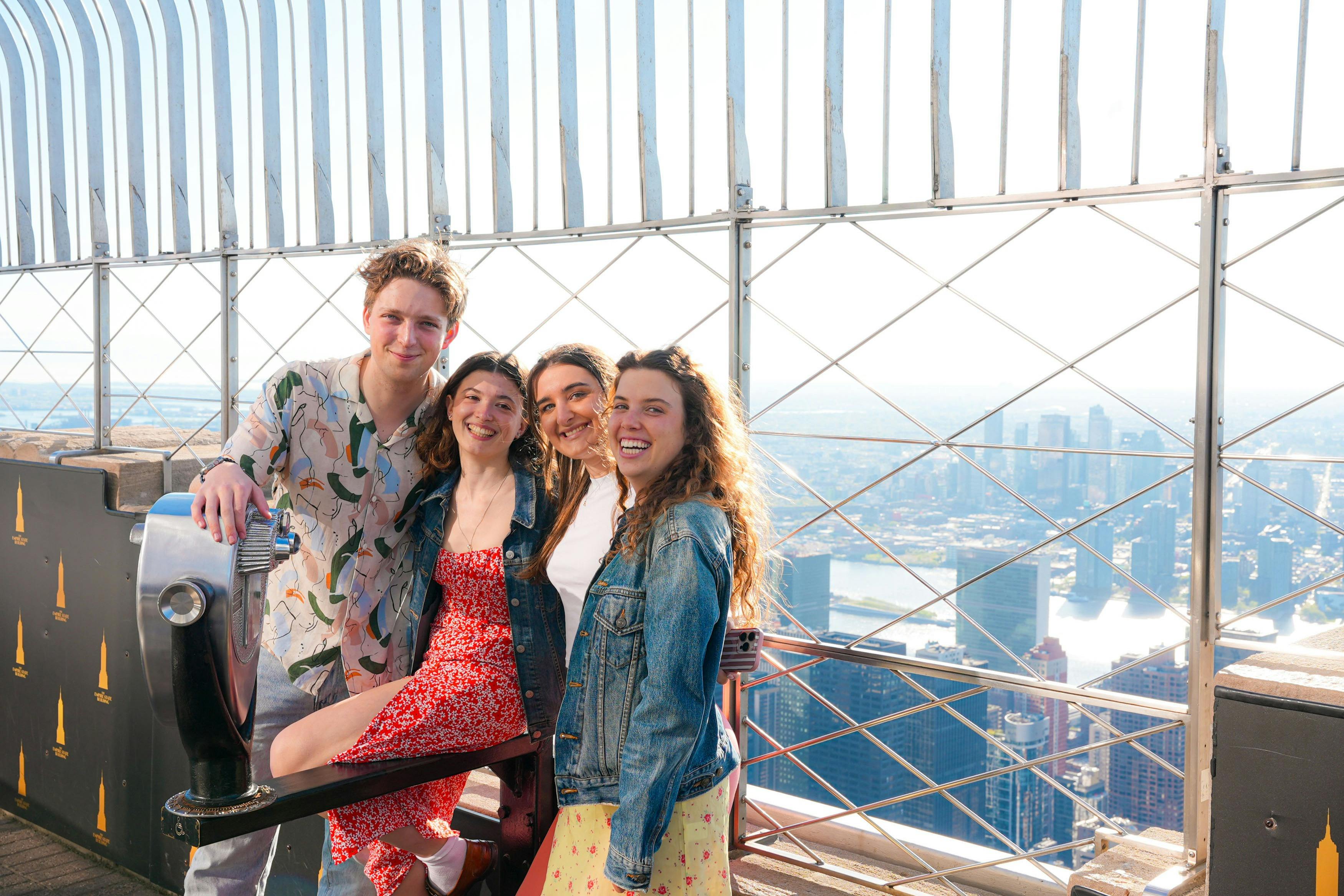 Quattro persone sorridenti in posa davanti a un visore a gettoni su una piattaforma panoramica, con il panorama della città sullo sfondo.