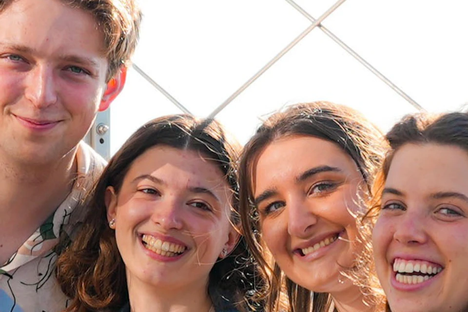 Four smiling people posing by a coin-operated viewer on an observation deck with a cityscape visible in the background.