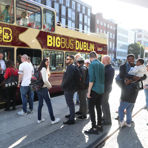People wait in line to board a double-decker sightseeing bus labeled "Big Bus Dublin" on a sunny street in the city.