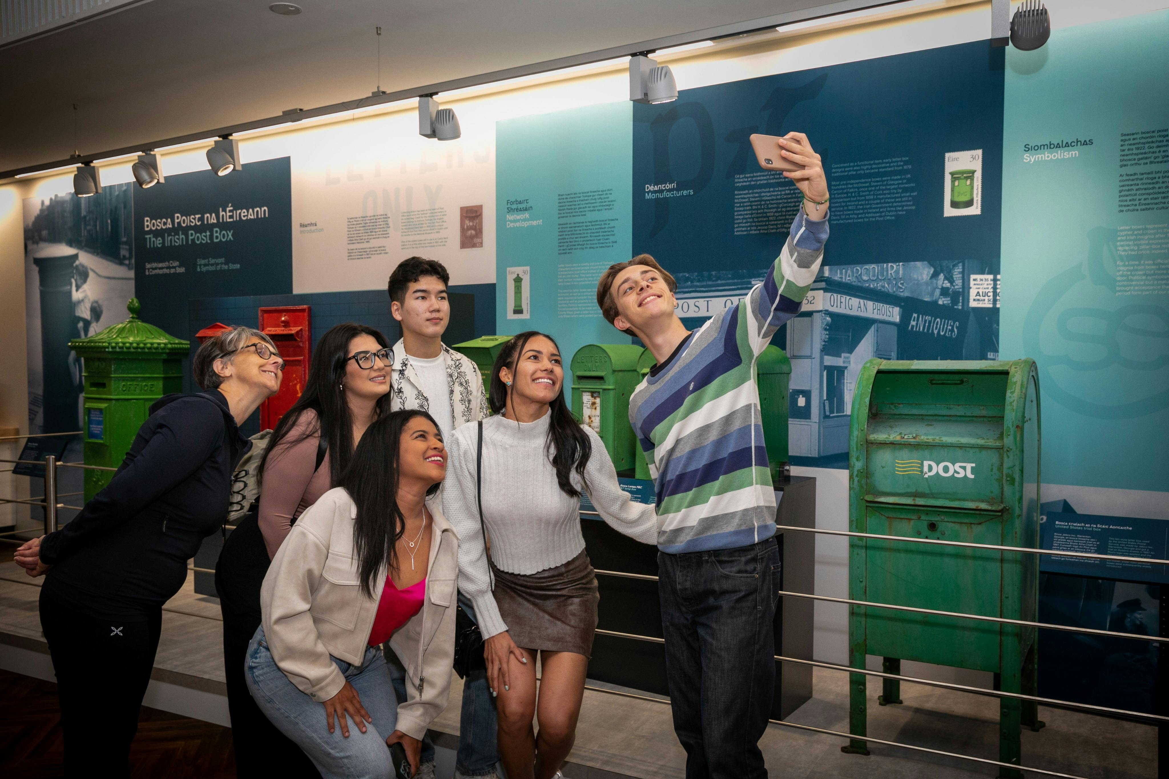 Eine Gruppe von fünf Personen, die lächelnd ein Selfie vor einem Display mit verschiedenen Postboxen machen.