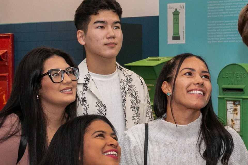 A group of five people smiling and taking a selfie in front of a display of various postal boxes.