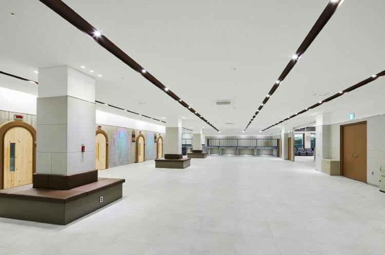 Spacious modern interior with white floors, benches, wooden doors, and ceiling lights. No people are present.