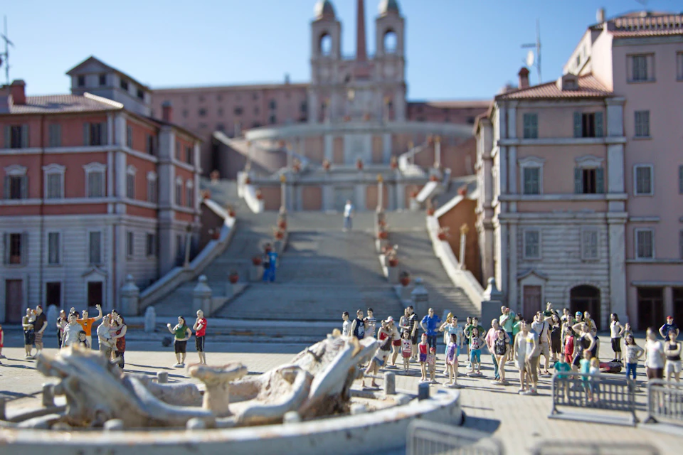 A detailed model of a city square with a fountain, stairs, and miniature figures representing people in a public space.