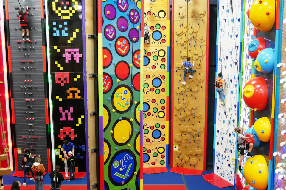 Colorful indoor climbing walls with various designs and people climbing. The walls feature patterns and interactive elements.