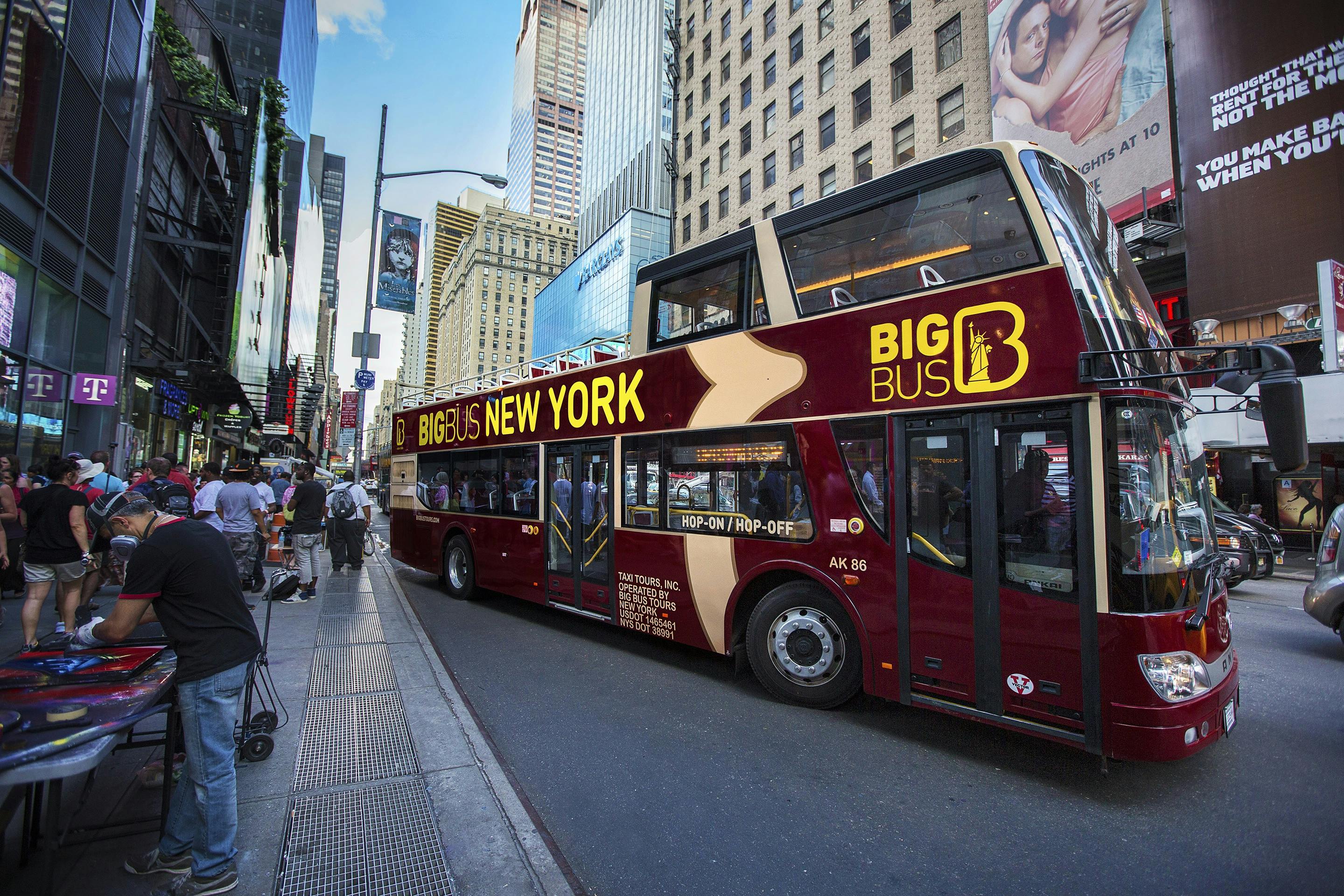 Un bus touristique à deux étages portant l'inscription "Big Bus New York" dans une rue animée de la ville, avec de grands immeubles et des piétons à proximité.