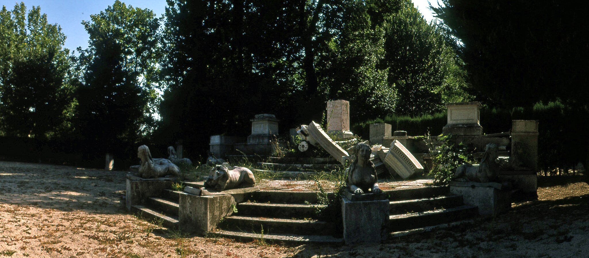 石阶上有破碎的墓碑和狮身人面像，周围环绕着杂草丛生的植被和树木。