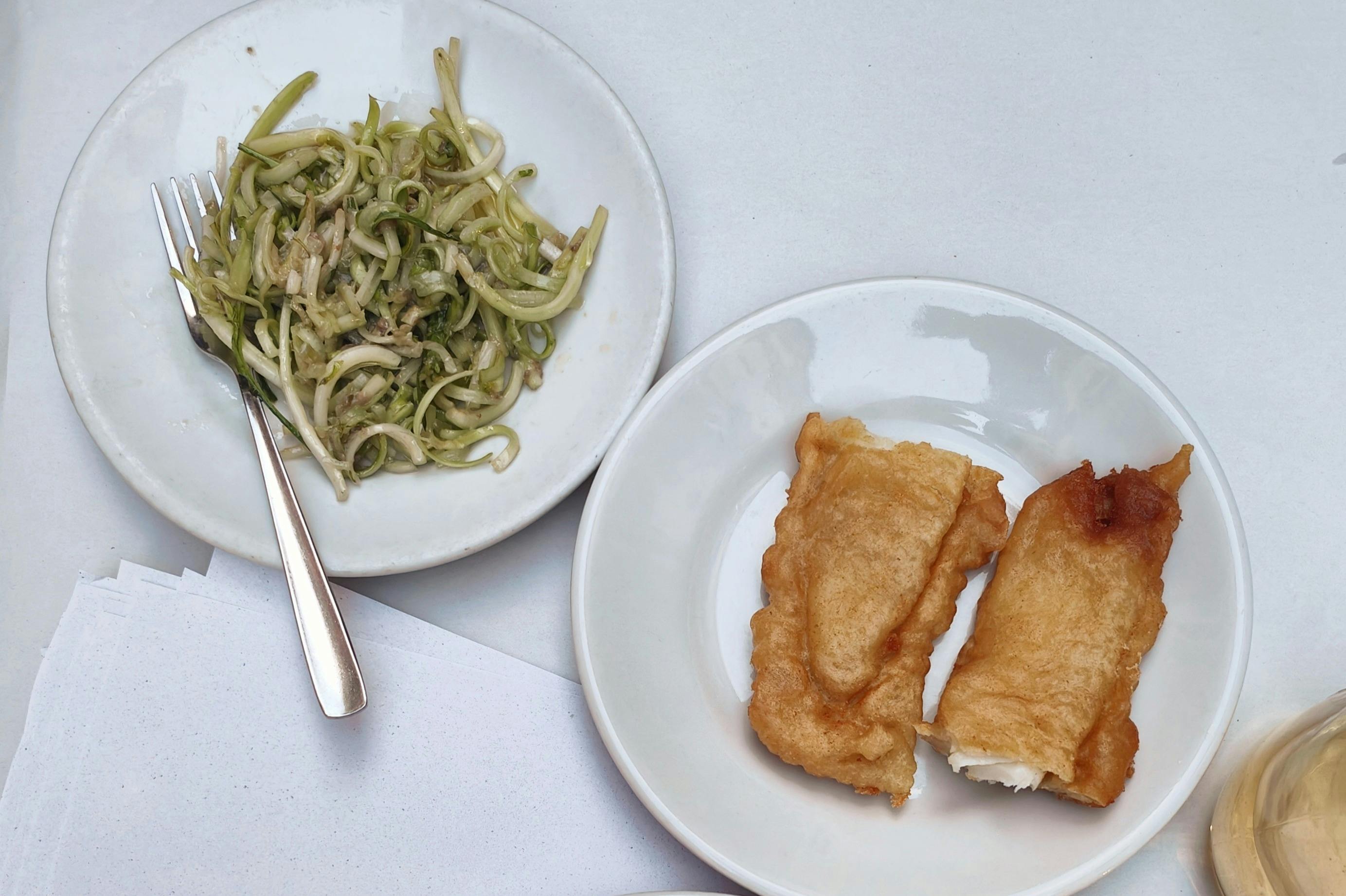 Two plates on a table; one with zucchini noodles and a fork, the other with two pieces of fried food.