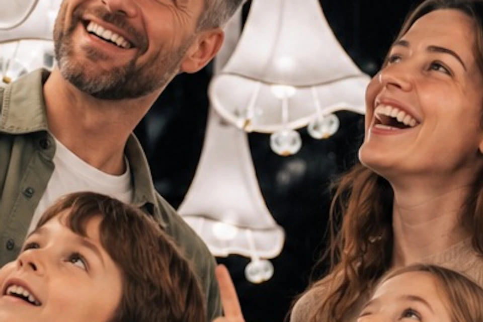 A smiling family of four interacts with hanging white lamps in a decorative display, appearing joyful and engaged.
