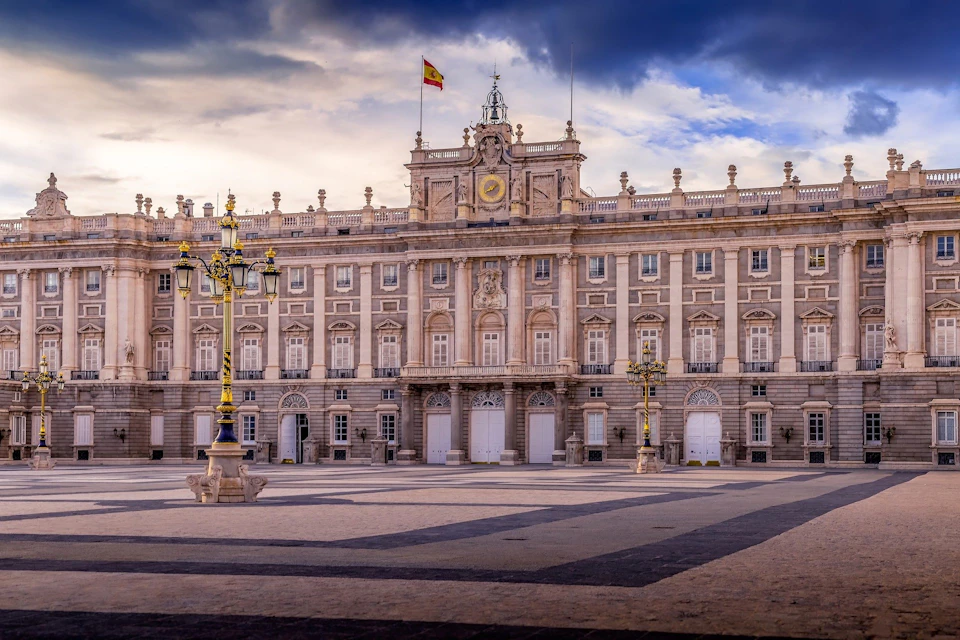 Majestic palace with symmetrical architecture, intricate details, lampposts, and an ornate clock, under a partly cloudy sky.
