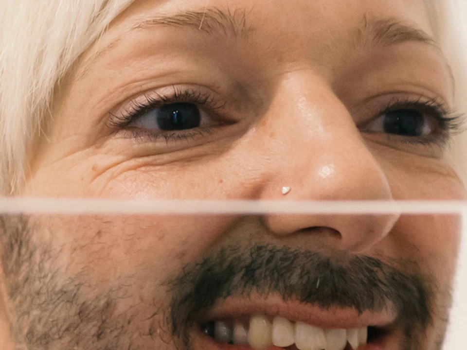 Person with short hair and a mustache looks into a segmented mirror, causing their reflection to appear fragmented.