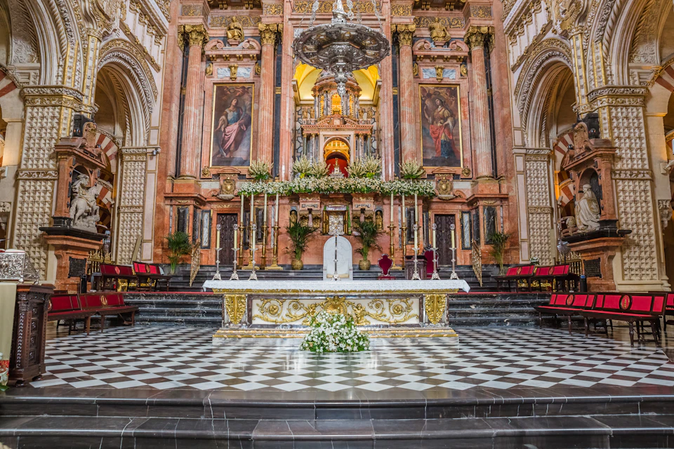 Ornate church altar with golden details, floral decorations, religious paintings, and a checkered floor, set against a grand backdrop.