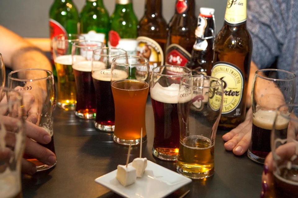 Various beer bottles and half-filled beer glasses on a table with a small plate of cheese cubes on toothpicks.