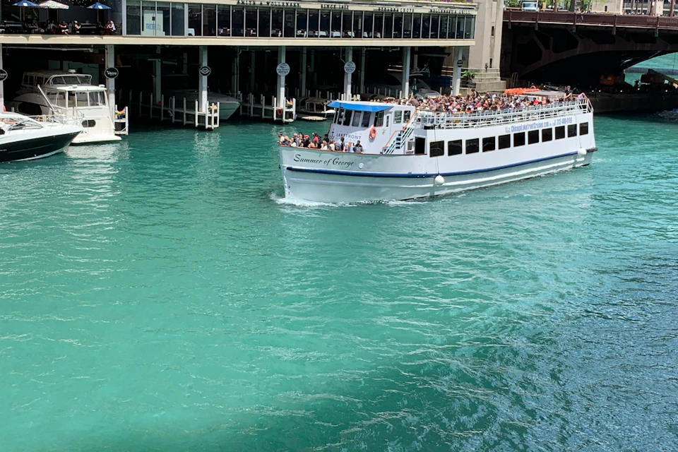 A white tour boat named 'Summer of George' on a turquoise river near a building with docks.