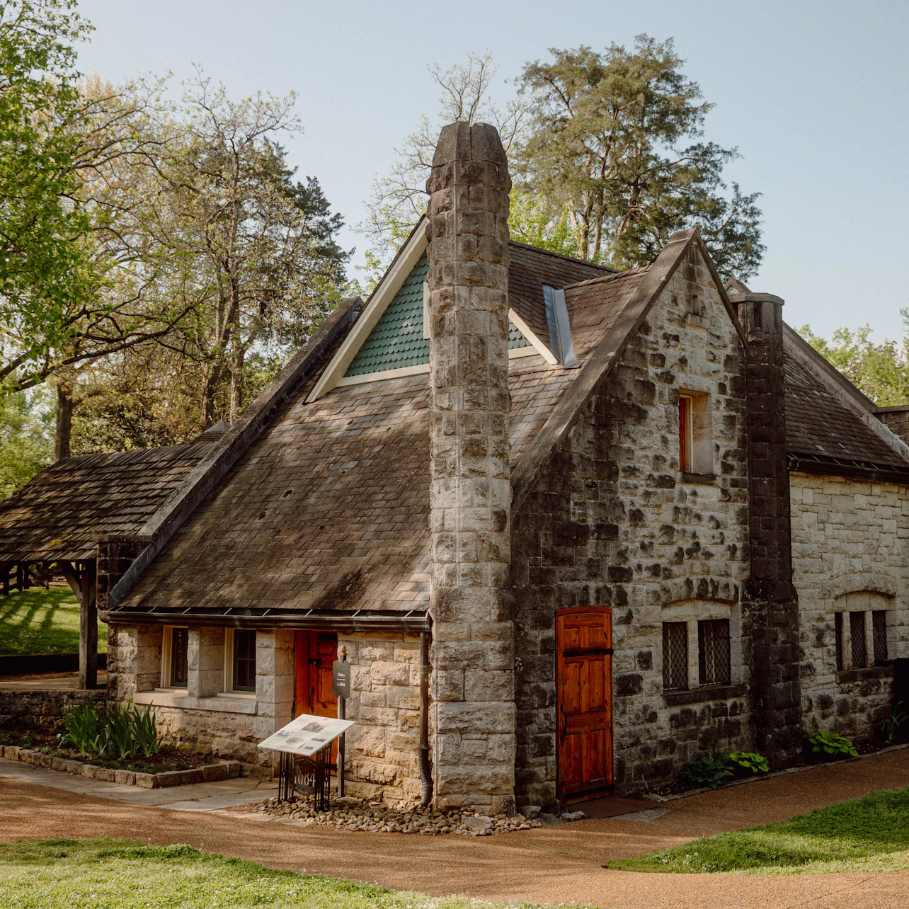 A stone cottage with a steep roof, red door, chimney, and trees in the background on a sunny day.