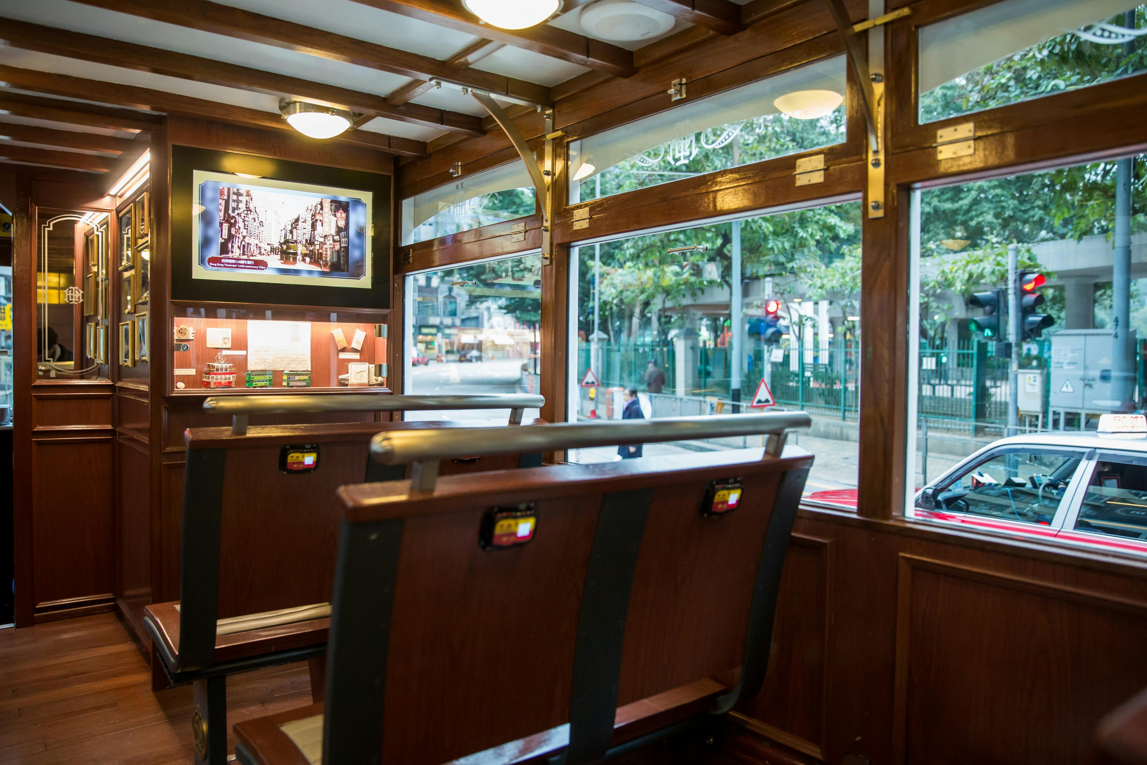 Interior of a tram with wooden seats, windows displaying a street view, and a screen showing an image inside.