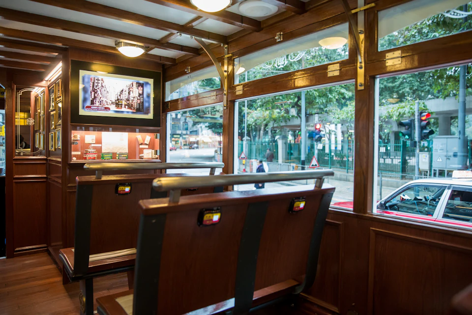 Interior of a tram with wooden seats, windows displaying a street view, and a screen showing an image inside.