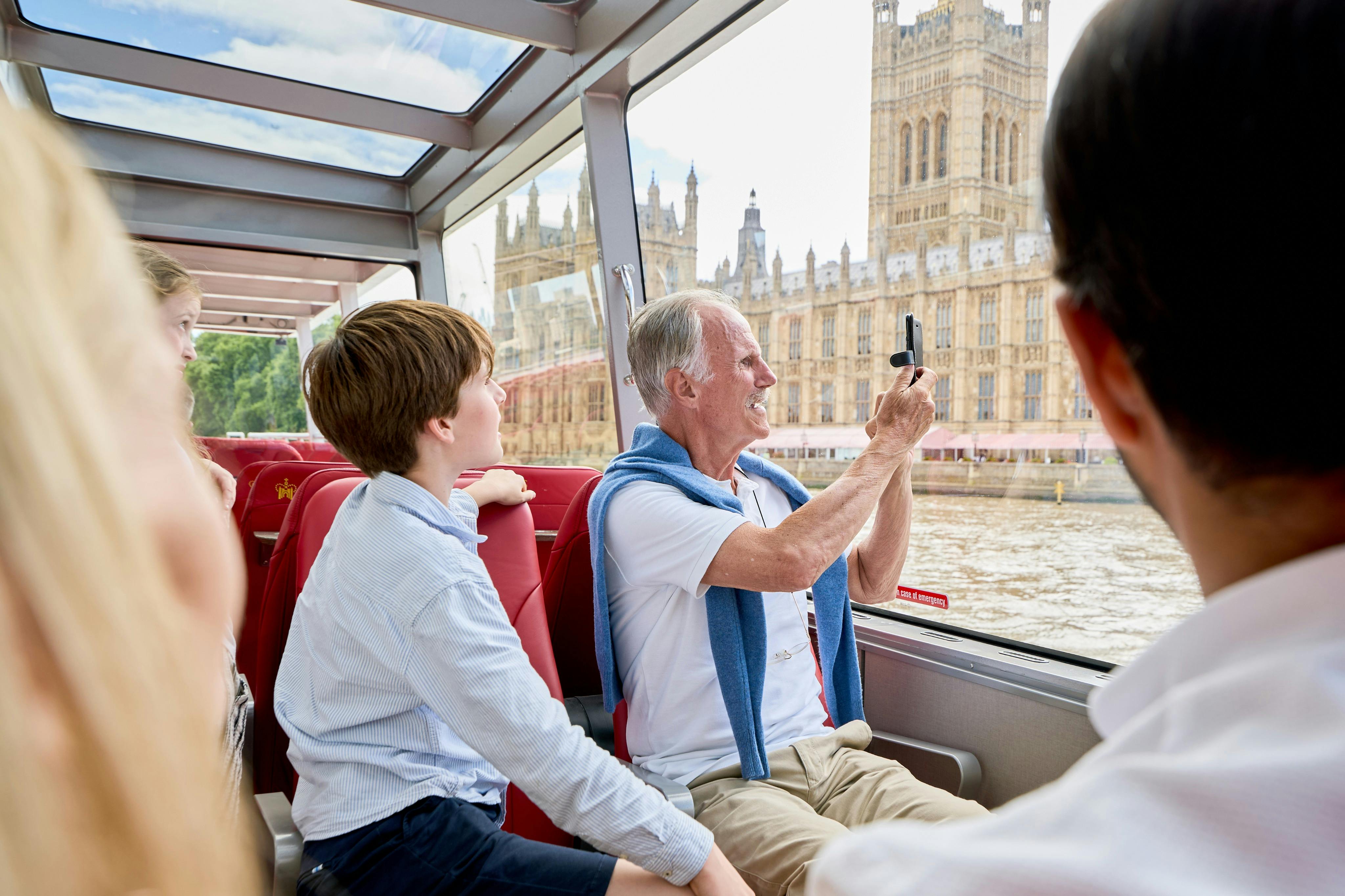 Un groupe de personnes à bord d'un bateau, dont l'une prend une photo du palais de Westminster à Londres à travers la vitre.